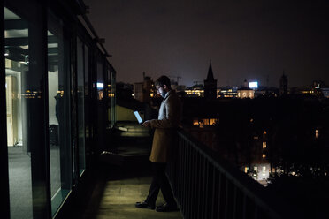 Mid adult businessman looking at laptop on office balcony at night - CUF51341