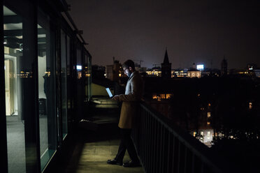 Mittlerer erwachsener Geschäftsmann, der nachts auf dem Balkon seines Büros auf seinen Laptop schaut - CUF51341