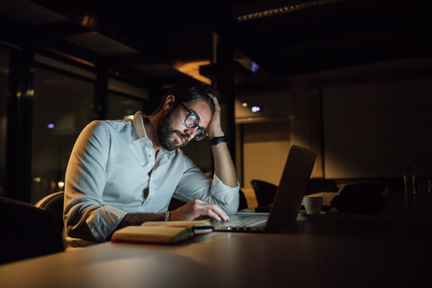 Müder Geschäftsmann, der nachts im Büro auf seinem Laptop tippt, lizenzfreies Stockfoto