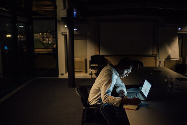 Junger Geschäftsmann, der nachts im Büro Notizen auf dem Laptop macht - CUF51369