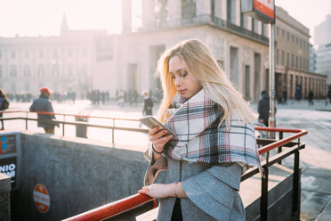 Young woman looking at smartphone by underground station, Milan, Italy - CUF51371