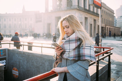 Junge Frau schaut in der U-Bahn-Station auf ihr Smartphone, Mailand, Italien - CUF51371