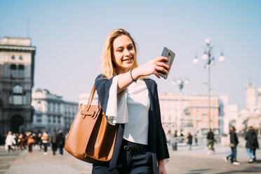 Young female tourist taking smartphone selfie in city square, Milan, Italy - CUF51377