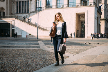 Junge Frau spaziert auf einem Stadtplatz und schaut auf ihr Smartphone - CUF51378