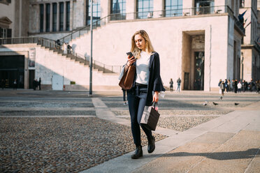 Young woman strolling in city square looking at smartphone - CUF51378