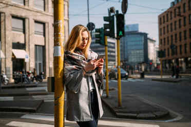 Junge Touristin, die an einer Straßenbahnhaltestelle auf ihr Smartphone schaut, Mailand, Italien - CUF51382