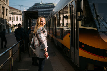 Junge Frau, die an einer Straßenbahnhaltestelle über ihre Schulter schaut, Porträt, Mailand, Italien - CUF51385