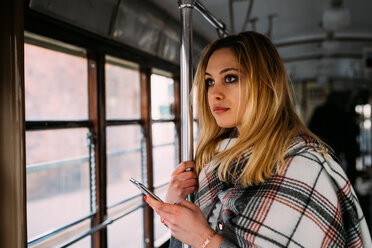 Junge Frau mit Smartphone schaut aus der Straßenbahn - CUF51387
