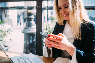 Young woman at sidewalk cafe table looking at smartphone - CUF51389