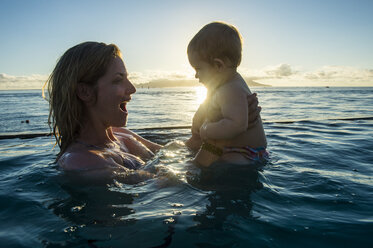 Französisch-Polynesien, Tahiti, Papeete, Frau spielt mit ihrem kleinen Baby in einem Infinity-Pool bei Sonnenuntergang - RUNF02058