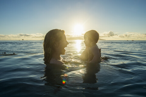 Französisch-Polynesien, Tahiti, Papeete, Frau spielt mit ihrem kleinen Baby in einem Infinity-Pool bei Sonnenuntergang, lizenzfreies Stockfoto