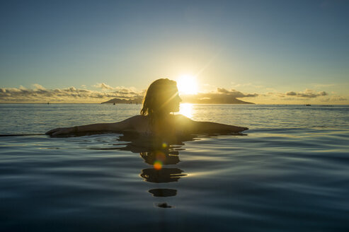 French Polynesia, Tahiti, Papeete, woman enjoying the sunset in an infinity pool - RUNF02060