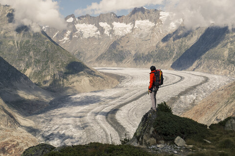 Kaukasischer Mann steht auf einem Felsen in verschneiten Bergen, lizenzfreies Stockfoto