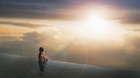 Chinese woman in infinity pool admiring sunset - BLEF03274