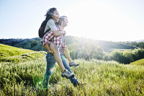 Smiling Man carrying girlfriend piggyback on hill stock photo
