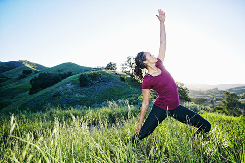 Gemischtrassige Frau übt Yoga auf einem Hügel, lizenzfreies Stockfoto