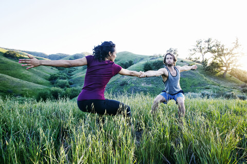 Paar hält sich an den Händen und praktiziert Yoga auf einem Hügel, lizenzfreies Stockfoto