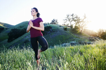 Gemischtrassige Frau übt Yoga auf einem Hügel - BLEF03314