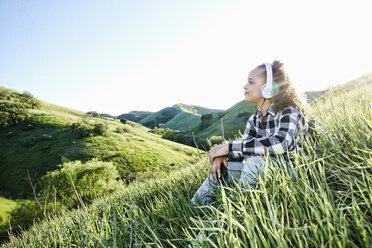 Girl sitting on hill listening to headphones - BLEF03326