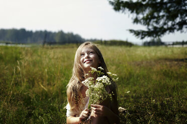 Caucasian girl holding bouquet of wildflowers in field - BLEF03363