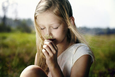 Caucasian girl smelling wildflower in field - BLEF03364