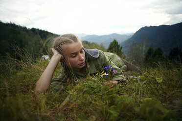 Caucasian girl holding wildflowers laying in grass on hill - BLEF03375