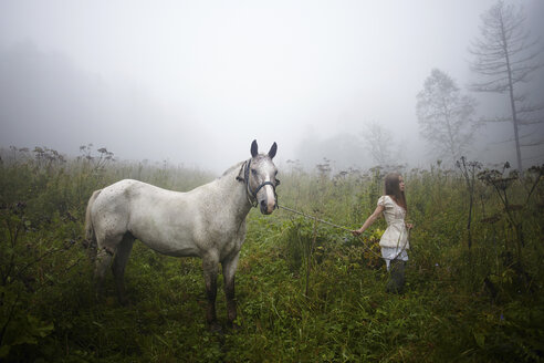 Kaukasisches Mädchen geht mit Pferd im nebligen Feld spazieren - BLEF03377