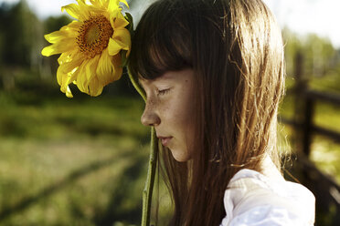 Profil eines kaukasischen Mädchens mit Sommersprossen, das eine Sonnenblume hält - BLEF03382