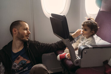 Little girl watching movie on screen during a flight while her father taking care - GEMF02952