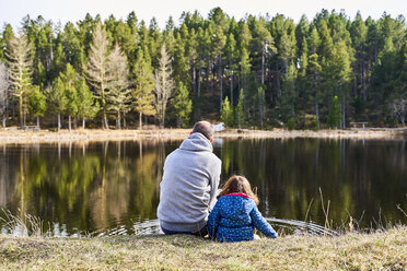 France, Pyrenees, back view of father and little daughter sitting side by side in front a lake - GEMF02959