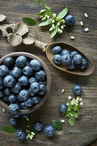 Schale mit Heidelbeeren, Holzlöffel, Heidelbeerblüten auf Holz, lizenzfreies Stockfoto