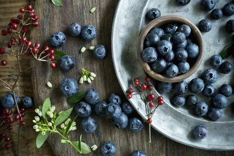 Schale mit Heidelbeeren, Holzlöffel, Hagebutte, Heidelbeerblüten auf Holz, lizenzfreies Stockfoto