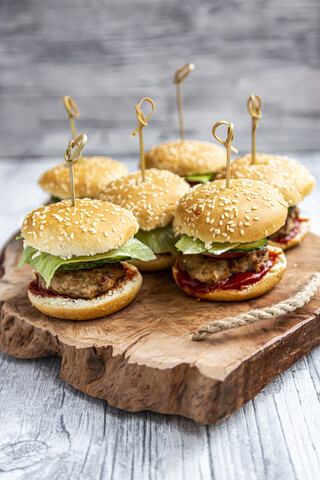 Mini-Burger mit Hackfleisch, Salat, Gurke und Tomate auf Holztablett, lizenzfreies Stockfoto