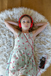 Girl lying on carpet at home listening to music with headphones and smartphone - SARF04280