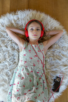 Mädchen liegt zu Hause auf dem Teppich und hört mit Kopfhörern und Smartphone Musik - SARF04280