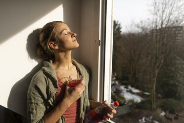 Junge Frau am Fenster genießt den Sonnenschein - GUSF01963