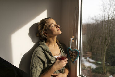 Junge Frau am Fenster genießt den Sonnenschein - GUSF01964