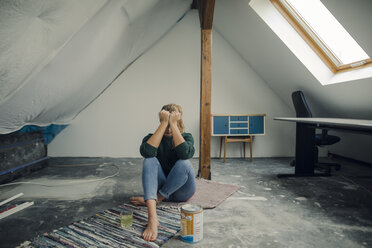 Frustrierte junge Frau, die mit einem Farbeimer auf dem Boden eines Dachbodens sitzt - GUSF01980