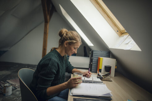 Junge Frau sitzt an einem Schreibtisch auf dem Dachboden und studiert einen Ordner - GUSF01984