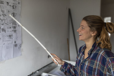 Glückliche junge Frau studiert die Montageanleitung an der Wand - GUSF02001