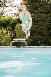 Kaukasisches Mädchen, das sich die Nase hält und vom Sprungbrett ins Schwimmbad springt - BLEF03445