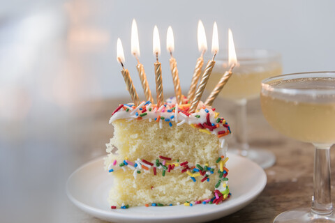 Kerzen brennen auf einem Stück Kuchen mit Streuseln in der Nähe von Champagner, lizenzfreies Stockfoto