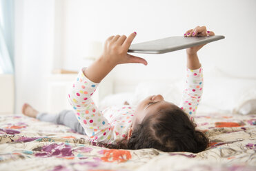Gemischtrassiges Mädchen auf dem Bett liegend mit digitalem Tablet - BLEF03453