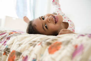 Smiling Mixed Race girl rolling on bed - BLEF03454
