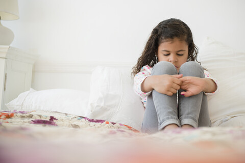Unglückliches Mixed Race Mädchen sitzt auf dem Bett, lizenzfreies Stockfoto