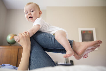 Caucasian mother laying on bed balancing baby son on legs - BLEF03464