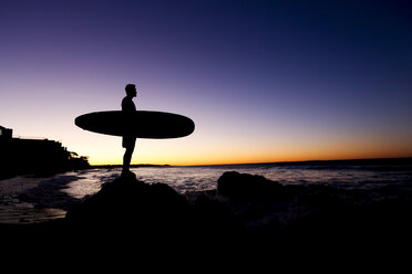 Silhouette of Hispanic man holding surfboard at beach - BLEF03472