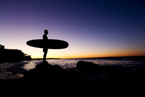 Silhouette of Hispanic man holding surfboard at beach - BLEF03472