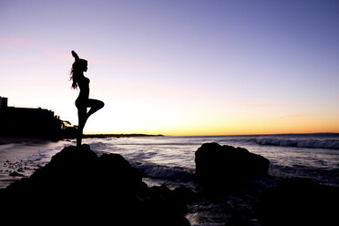 Silhouette of Caucasian woman balancing on rock at beach - BLEF03473