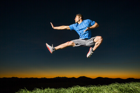 Kaukasischer Mann springt bei Sonnenuntergang, lizenzfreies Stockfoto